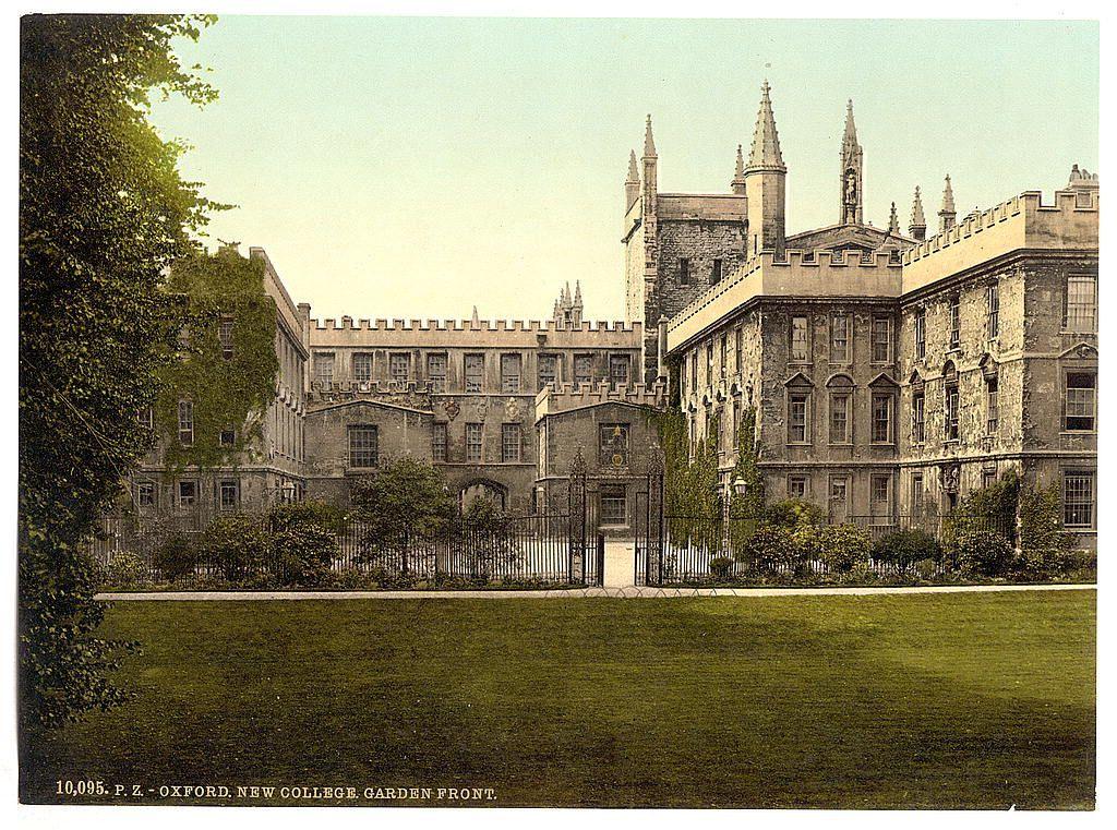 This image depicts a historical building, likely associated with an educational institution given the text "Oxford New College Garden Front." The architecture is characterized by Gothic revival elements such as pointed arch windows and ornate masonry. A lush green lawn stretches in the foreground, bordered by mature trees that suggest maturity of both age and establishment. In front of a large stone wall stands what appears to be an iron gate or fence, leading into the courtyard area. The structure is multi-storied with several chimneys visible, indicating multiple rooms within. Notably, there are no people present in this photograph, placing full emphasis on the architectural features.