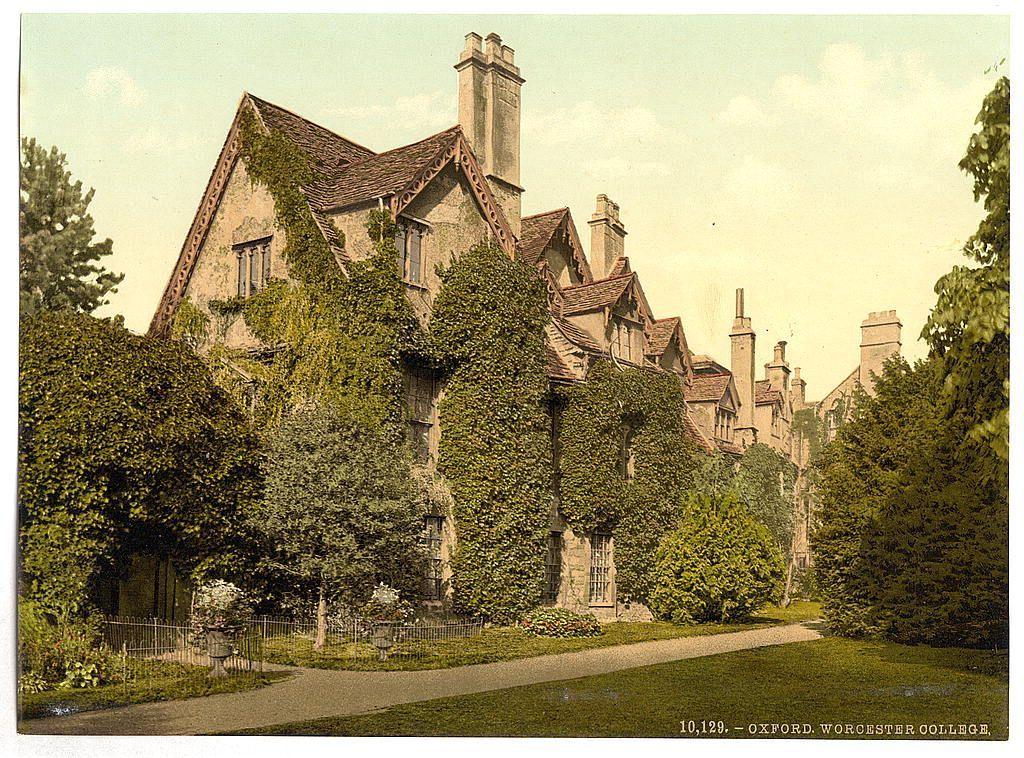 The image depicts a historic building, likely an old college or manor house associated with Worcester College at Oxford. The architecture is characterized by steeply pitched roofs and ornate woodwork on the gables. Ivy-covered walls give it a rustic appearance amidst mature trees. A well-maintained lawn leads to pathways lined with greenery and urns containing flowering plants, indicating garden landscaping designed for aesthetic pleasure or academic reflection.

The photograph's sepia tone suggests an age that aligns with its likely origins in late 19th-century England when such color printing was prevalent. This period is known for the widespread adoption of photochrom techniques to create detailed images from glass plate negatives on paper, a popular medium before modern photography emerged fully as we know it today.

The image captures not just a building but an era and setting rich in historical significance. It represents both architectural heritage and institutional life at its zenith during this period within academia.
