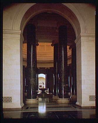 The image depicts a grand, neoclassical interior featuring tall columns with dark bases and lighter tops. These structural elements frame the view of an expansive hall that extends into the distance where another set of smaller ornate pillars can be seen at some depth away from the viewer's perspective. The architecture suggests a significant public or governmental building, possibly designed in early 20th century revivalist style.

The flooring is composed of large marble slabs laid out diagonally to create a pattern that radiates outward towards the vanishing point where the pillars meet on the distant wall. Above and beyond this central hall appears an arched passageway leading further into what seems like additional galleries or rooms, hinting at more architectural grandeur.

The color palette is muted with earthy tones of brown from the columns' stone contrasting against lighter shades in the marble floor and structural elements above. The overall impression conveyed by this photograph evokes a sense of awe-inspiring scale and historical significance befitting an institution like a national gallery or museum, as referenced in the provided caption.

The image is credited to Horydczak, who appears to have been active around 1920-1950. This suggests that he might have worked for such prestigious institutions during this period and had captured their architectural splend [...]