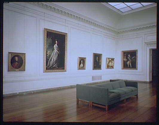 The image depicts a spacious gallery with white walls and wooden flooring, featuring an arrangement of classical-style paintings on the wall. The room is illuminated by natural light from a skylight in the ceiling. In total, six framed portraits are visible: two large-scale works prominently displayed against the back wall, accompanied by four smaller pieces placed at eye level along each side.

A green sofa with wooden legs sits in the center of the floor space, providing a comfortable viewing area for visitors to sit and contemplate the artworks. The overall atmosphere suggests an elegant setting dedicated to art appreciation, possibly part of a museum or private collection exhibit.

The painting is identified as Horydczak by Theodore (theo) approximately between 1890-1971 according to information found in National Gallery of Art English Painting ca. 1920-ca.