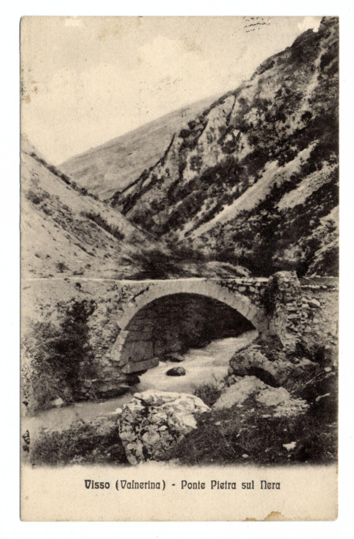 The image displays a vintage black-and-white photograph featuring an old stone bridge with multiple arches spanning over water, which appears to be flowing. The setting is rugged and mountainous, suggesting that the site could be in a valley or between elevated terrain. There are indications of wear on both the structure and landscape, such as exposed stones at the base of the walls and natural debris around the area where the bridge meets land.

The photograph has been printed with text overlaying it; however, due to image quality constraints, some parts may not be entirely legible without specific context. The visible part reads "Visso (Valnerina) - Ponte Pietra sul Nera," which likely identifies the location as Visso in Valnerina and refers to a stone bridge over an unnamed river or stream.

This type of image is often associated with historical records, travel memorabilia, or postcards from earlier periods. It evokes a sense of history and provides insight into past architecture and natural landscapes captured through photographic means at that time period.