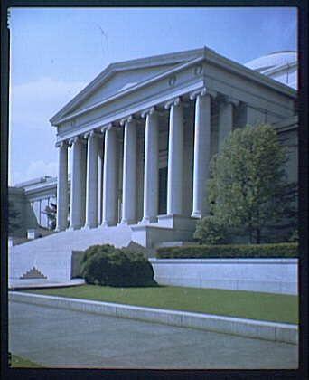This image shows the exterior of a neoclassical building with a prominent portico featuring six tall, white columns. The architecture suggests an institutional or governmental structure, reminiscent of Greek temples. In front of the entrance is well-maintained greenery, including shrubs and manicured lawns, indicating that this location may be significant in terms of landscaping as well as its architectural style.
The photo appears to have a vintage quality with faded colors, suggesting it could date back several decades ago, possibly around 1920-50. The image is likely part of the National Gallery of Art collection and was taken from Constitution Avenue II.