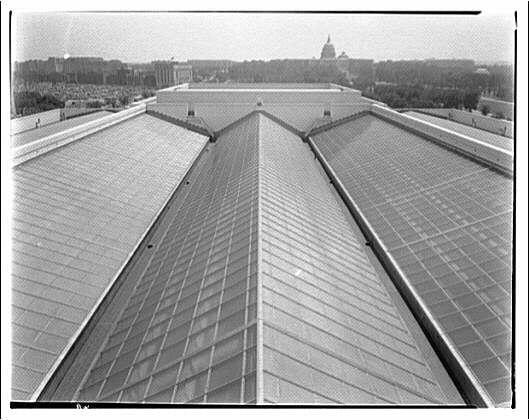 The image depicts a large, expansive roof with multiple triangular sections converging towards the center where it seems to form an apex. The structure appears modern and is likely made of metal or some other durable material. In the background, there are trees lining what looks like parkland, followed by rows upon rows of buildings that extend into the distance under a somewhat overcast sky.

The photograph is in black-and-white which suggests it may be quite old, potentially even dating back to early 20th-century times as indicated by its source. It's mentioned that this photo relates to "International Nickel Co." and was captured around "ca. 1920-ca. 1950," placing the image in a historical context.

Further information about the photographer, Theodor Horydczak (approximately 1890-1971), can be found at National Gallery of Art where additional details and artworks by this artist may also reside.

The specific reference to "Roof of National Gallery of Art" implies that one or more portions of the roof design might have been inspired, constructed using materials from, or associated with International Nickel Co., a company known for its contributions to steelmaking in early 20th-century America.
