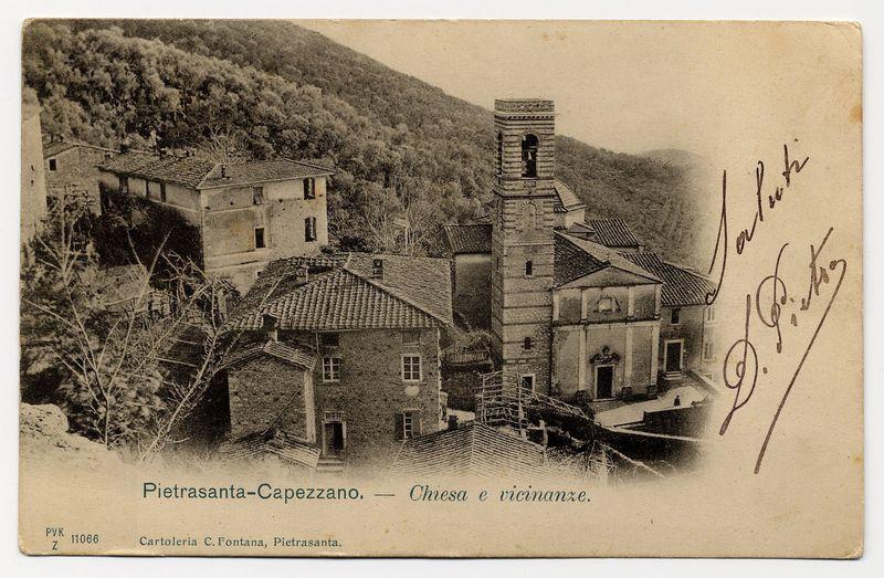 The image displays an old postcard featuring a monochromatic photograph of the town Pietrasanta-Capezzano, with a focus on its church and surrounding area. The top left corner bears handwritten inscriptions in cursive script that appears to be signatures or initials, potentially those who created or sent the card.

In the center is a detailed depiction of buildings characteristic of rural Italian architecture from an earlier era. Prominent structures include what seems like residential houses with pitched roofs made from tiles and brickwork chimneys protruding into the sky. To the right stands a prominent church tower that reaches higher than the surrounding dwellings, indicating its significance as both architectural and social center in this setting.

The background reveals lush greenery indicative of a mountainous or hilly region, providing context to Pietrasanta-Capezzano's geographical location. The bottom left corner includes text identifying "Pietrasanta-Capezzano — Chiesa e vicinanza," which translates from Italian as "Church and vicinity" in English.

Additional information on the postcard indicates it is part of a collection known as 'Cartoleria C.Fontana, Pietrasanta,' with reference numbers PVK 11066 Z. A URL provided suggests that further details or images related to this subject can be found online at the given web address. The overall impression conveyed by [...]