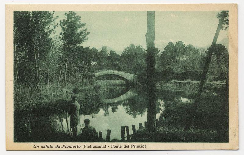 The image is a vintage postcard depicting a serene natural scene. In the foreground, two figures appear to be standing on a wooden platform or bridge that spans across calm water, which reflects their silhouettes and some of its surroundings.

In the midground, there's another individual sitting by the edge of the same body of water. The background features dense vegetation with various trees partially obscuring the view. Notably, in the center distance is a picturesque arched bridge crossing over the landscape, connecting two parts of what seems to be an expansive wooded area.

The text at the bottom left corner reads "Un saluto da Fiumetto (Pietrasanta) - Fonte del Principe," which translates from Italian as "A greeting from Fiumetto (Pietrasanta) - Fountain of the Prince." The watermark or logo in the lower right indicates it's associated with Eden Park. The overall coloration is muted, with a sepia tone suggesting age and giving the photograph an antique feel.

This image captures a tranquil moment by what appears to be "Fiumetto," likely referring to Fiumetto Beach (also known as Portovenere), which has historical significance in Pietrasanta, Italy, near Forte del Principe. The landmark mentioned suggests this could have been taken during the late 19th or early 20th century when such postcards were popular for conveying one's experiences to distant loved ones and fri [...]