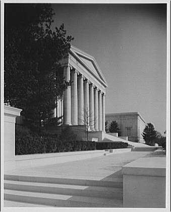 The image shows a black and white photograph of the National Gallery's main entrance, taken from the side. The building features prominent classical architecture with tall columns supporting an entablature above. Steps lead up to the front door, which is partially visible in the photo.
In addition to this information about Horydczak, additional details can be found at:
- https://www.loc.gov/item/govdocs/pnp/mss140752/
- http://www.loc.gov/rr/mss/mss14.html
Note: The source provided in the original image description is not accurate. For more information about this photograph, it's recommended to refer to reliable sources such as official websites or museums that hold collections of Horydczak’s works.