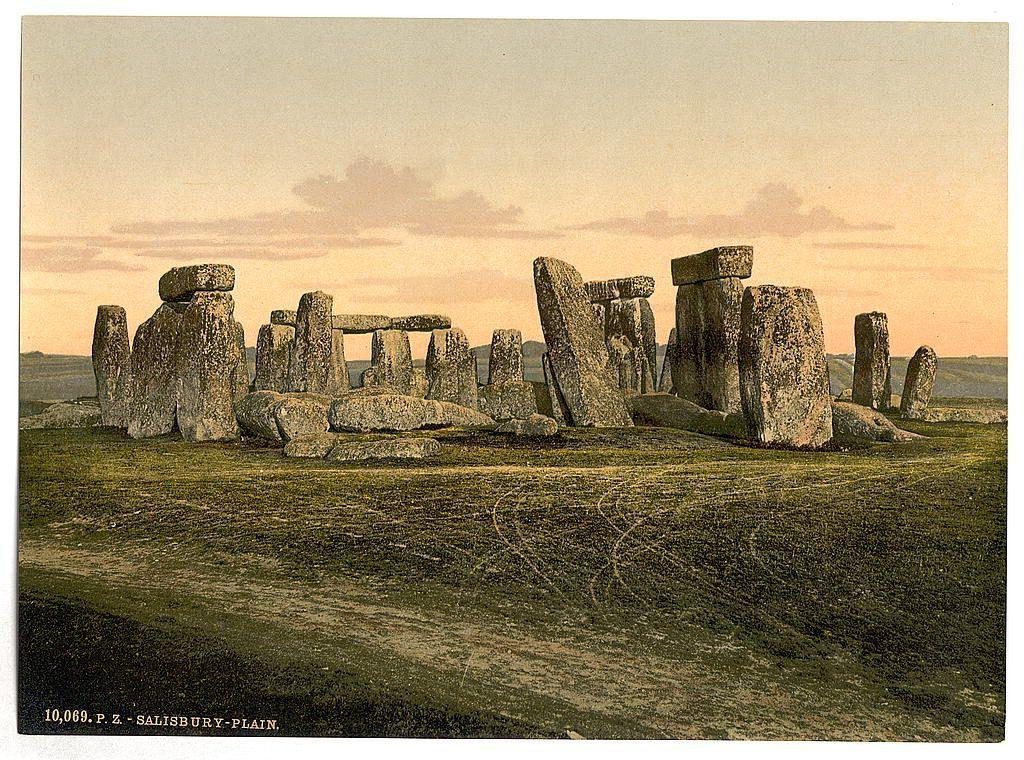 This image depicts Stonehenge, an ancient prehistoric monument located in Salisbury Plain, Wiltshire, England. The iconic structure consists of a circular arrangement of large standing stones, some positioned on top to form megalithic constructions or dolmens. In the photograph, we see these stones set against a backdrop of rolling hills and a soft-hued sky during what appears to be either sunrise or sunset. The colors range from warm yellows and oranges in the upper portion of the image to cooler greens and browns on the ground. This particular representation is rendered with an early photographic technique known as photochrom, which was popular for its ability to produce highly detailed images using hand-tinted paper prints. Given the reference information provided, it suggests that this specific print dates between approximately 1890 and 1900.