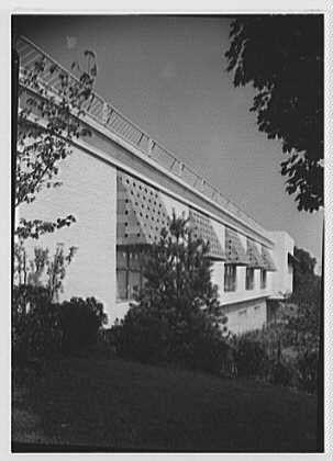The image shows a black and white photograph of an Art Deco style building, likely from the early 20th century. The structure features large windows with geometric patterns etched into them, as well as decorative awnings on some parts of the facade. Trees are visible in front of the building, suggesting that it is located near a park or wooded area.
This photograph was taken by Gottscho-Schleisner, Inc., who were known for their architectural photography during this period. The image appears to be part of Lord & Taylor's business records from Millburn, New Jersey and dates back to August 23rd, 1949. It is a safety negative measuring 5x7 inches in size.
Overall, the photograph captures an interesting example of mid-century architecture with its clean lines and modernist sensibility.