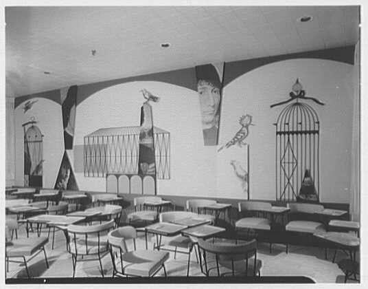 This image depicts an interior scene of a room with rows of empty school desks and chairs, suggesting a classroom setting. The walls are adorned with large murals featuring various elements such as human faces, architectural structures like arches and cages, musical instruments including flutes, and other abstract shapes and designs. Notably, there is a prominent birdcage in the upper right corner of the mural.

The photograph appears to be from an archive or historical collection, given its black-and-white quality and style. The text on the image provides additional context, indicating it's associated with Lord & Taylor business located in Bala-Cynwyd, Pennsylvania, specifically mentioning a date (1955 Apr 16) which may refer to when this mural was created or displayed.

The source of the photograph is attributed to Gottschol-Schleisner, Inc., and it's noted as one negative on safety film with dimensions specified as '4x5 in.' The URL provided suggests that more information about the image can be found at the given webpage.