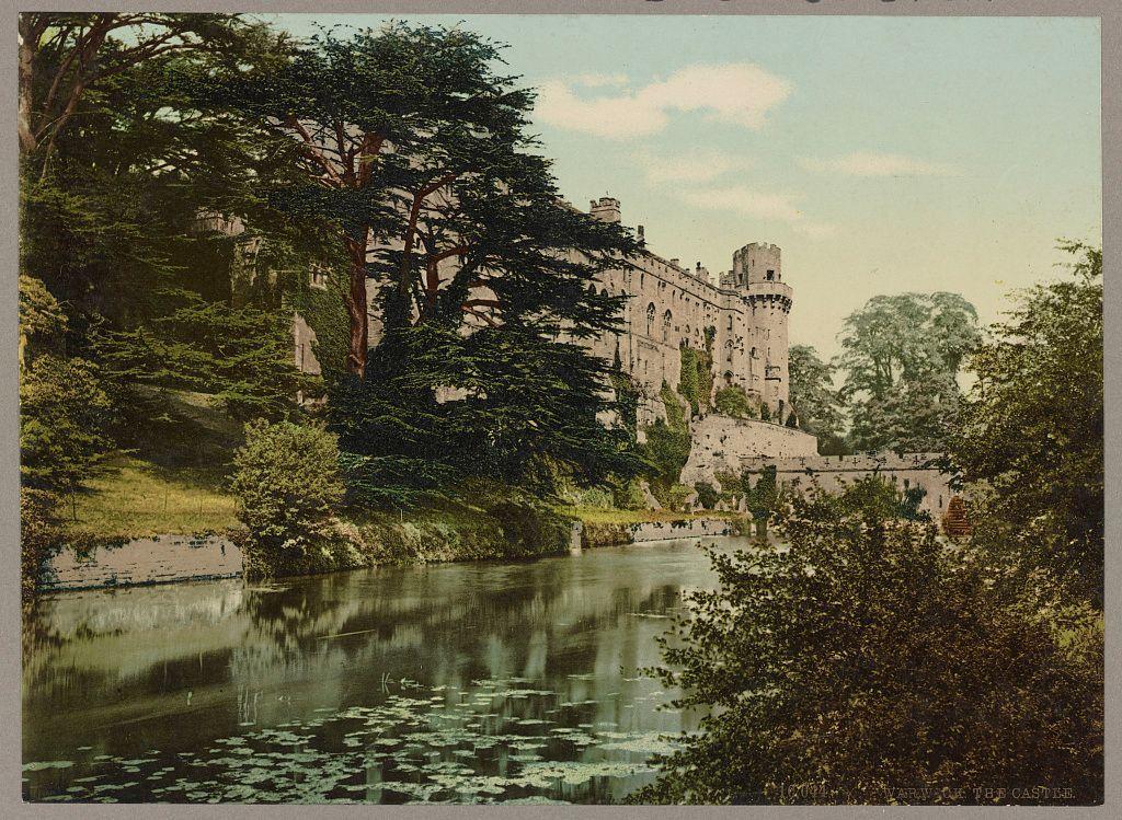 This image depicts a historic castle situated along the edge of a tranquil river, surrounded by lush greenery. The architectural style suggests it may be from medieval times, with various towers and battlements visible atop its walls. Ivy covers parts of the building's facade, blending nature seamlessly into the structure. Reflective water in the foreground hints at calm weather conditions, possibly early morning or late afternoon given the soft light quality. Overhanging trees frame the scene on both sides, indicating a secluded, picturesque setting likely to be found in Warwick Castle, England as referenced by the caption card mentioned in the provided link. The image carries an old postcard appearance with faded colors and textured edges that suggest its age or intentional vintage treatment for artistic effect.