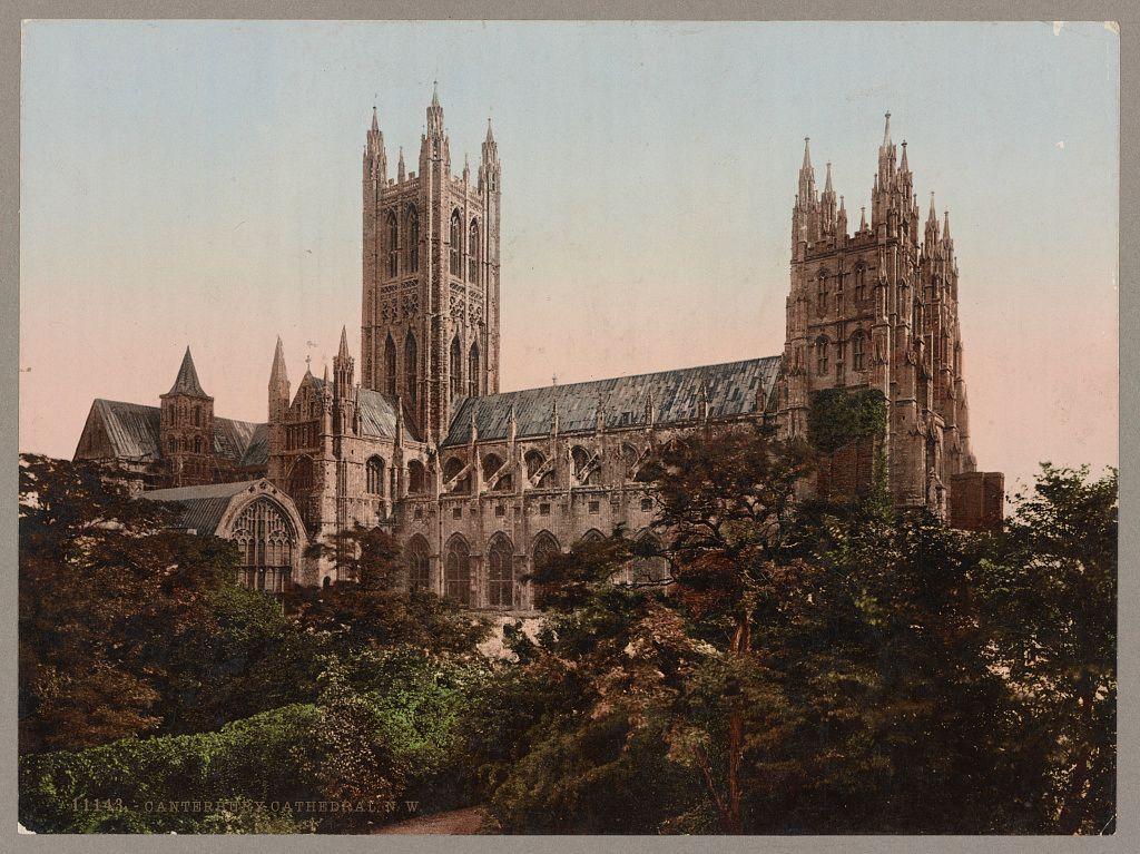 The image depicts a historic Gothic cathedral with intricate architecture, featuring tall spires and detailed stonework. The structure is surrounded by lush greenery, suggesting it's nestled within or near natural landscapes such as gardens or wooded areas. Its design includes large arched windows, pointed arches, ribbed vaults, and flying buttresses, characteristic of the Gothic style popular during medieval Europe.

The color palette has a sepia tone, indicating that this could be an old photograph or a vintage reproduction from around 1890-1900. This period was known for its production of photochrom prints, which were made by creating chromolithographs using photographic techniques to reproduce the hues and details seen in paintings.

The cathedral is identified as "Canterbury Cathedral" with a handwritten label at the bottom left corner indicating this specific landmark's name, further confirming its identity. The surrounding foliage appears well-maintained but not overly manicured, suggesting an effort to preserve natural beauty alongside historical preservation efforts.