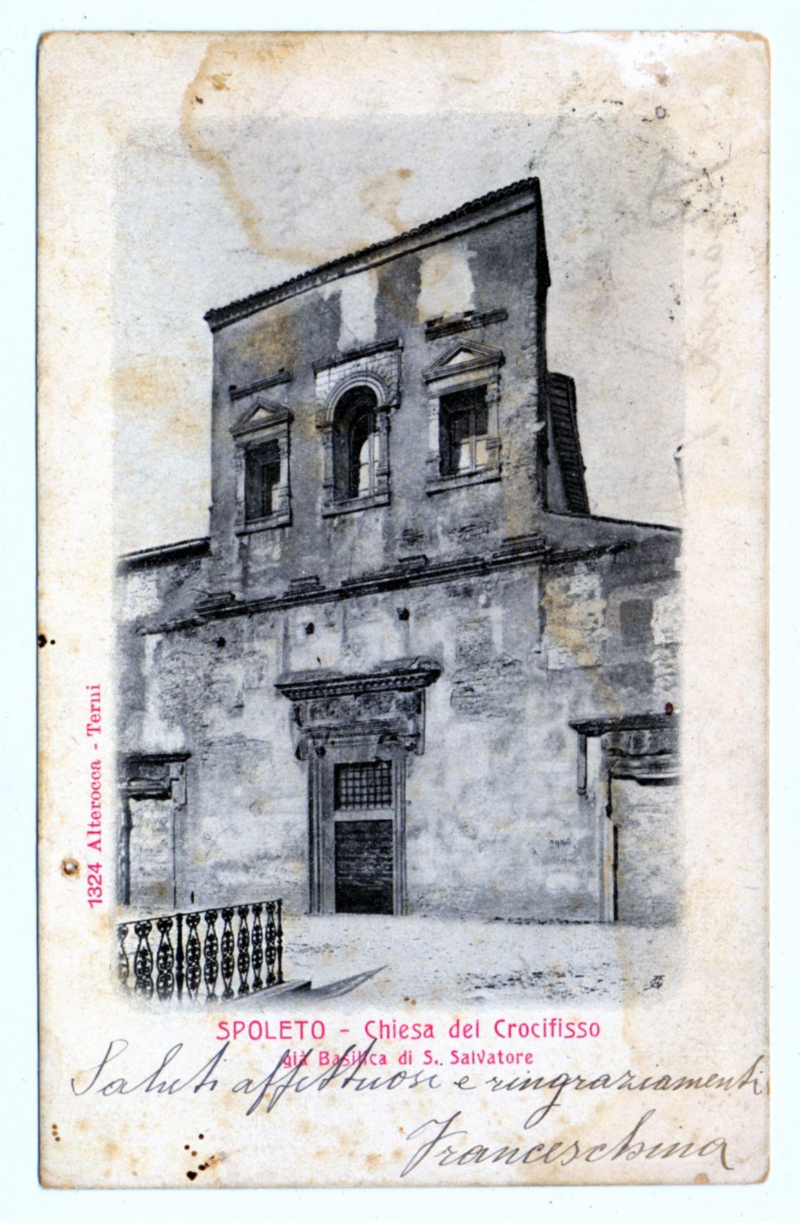 The image depicts a historical photograph of the Church of Crocefisso in Spoleto, as indicated by red text at the bottom. The building appears aged and weathered with visible wear on its facade, including discoloration and some deterioration. It features classical architectural elements such as arched windows, decorative cornices, and stone masonry work that suggests it is an old structure possibly dating back several centuries.

The photograph has a vintage look, enhanced by the sepia tone and signs of aging like creases or spots on its surface. There are handwritten annotations in red ink across the bottom right corner which seem to be signatures or notes related to the image's provenance. The background is plain white with no additional elements other than the church building.

The text also provides a date, 1324 Alterocca - Terui, and identifies 'Alteroca' as a place in Italy associated with this historical site. On closer inspection of the handwritten notes at the bottom right corner it appears to be Francesco Maria written on white paper.