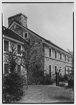This black and white photograph depicts an old stone building with multiple windows, a chimney on the upper right side, and what appears to be a small tower or extension at its peak. The structure is surrounded by trees, bushes, and shrubs in front of it, indicating that it might be located within a landscaped area such as a garden or park-like setting.
The image has been credited to Dr. A.C. Barnes' residence in Chester Springs, Pennsylvania with the date noted as August 20th, 1942. The photo is part of Gottschol-Schleisner's collection and shows one negative that measures 5x7 inches. For more information about this specific image or to explore additional photographs within Dr. Barnes' residence archive, visiting https://images.loener.nl/gottscho-schleisner/ might be a valuable resource.
This photograph captures the historical ambiance of an old building in its natural surroundings and highlights the architectural style prevalent during that period.