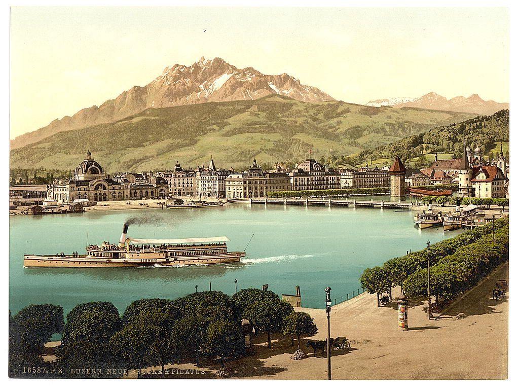 This postcard depicts a panoramic view of Lucerne, in the canton of Luzern (previously called as Lucerne) on Lake Lucerne. In this colorful photograph taken between approximately 1890 and 1900 by Keppler & Loenër's Photographic Workshops, you can see steamboat paddle-wheel vessels ferrying passengers across the lake to destinations in Switzerland’s Central Highlands. The boats are labeled "P.Z." (probably standing for "Postcard") on their side as well as with a number indicating that they were part of a fleet or collection.

Lucerne is nestled amidst magnificent Alpine scenery, and towering behind it sits Pilatus Mountain, its peak capped by snow even though the image appears to be taken in summertime. The town itself has an old-world charm, with European architecture lining both sides of the lakefront. Notable buildings include what looks like a grand railway station or hotel on the far left (possibly Station Luzern), and several well-preserved structures including mansions, public edifices, and possibly hotels.

The photograph is marked "16587 P.Z - LUCERNE NEUE FRÄULEIN & PILATUS" at its bottom right corner. It captures a bustling port scene with activity along the lakeside, where horse-drawn carriages are seen, indicating that this image dates from an era before automobiles were commonplace in Switzerland.

The photo has been printed on yellowed paper typical of early [...]