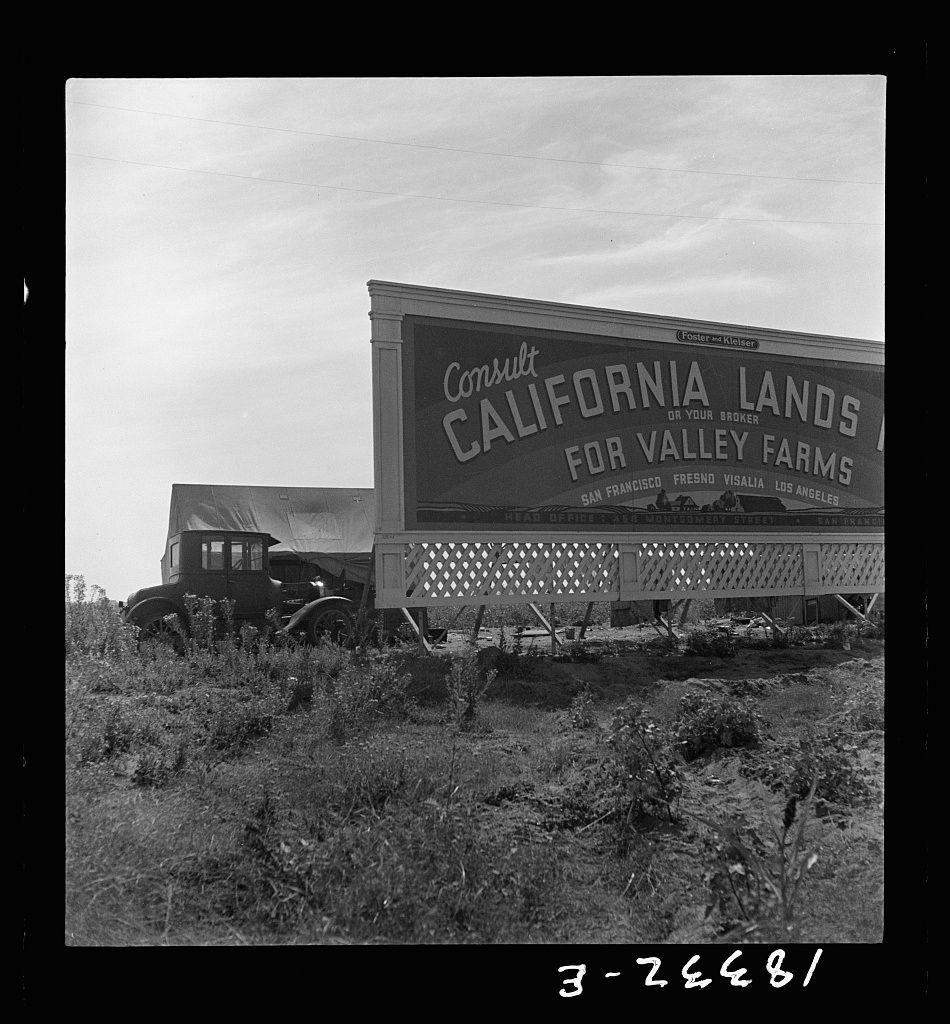 The image captures a scene dominated by an old-fashioned, large billboard reading "Consulate California Lands For Valley Farms." The signboard is situated along the side of what appears to be a rural highway. It's adorned with names like San Francisco, Fresno, Visalia, Los Angeles, and other cities which indicate its geographical reach for agricultural lands in these areas. Beneath it sits an old-fashioned truck that seems out of place amidst the barren landscape, possibly indicating transportation or services related to agriculture.

The ground beneath is dry and cracked, suggesting a lack of recent rainfall or arid conditions typical of California's Central Valley where such billboard advertisements would be pertinent for land sales in agricultural areas. The sky above appears overcast with thin clouds hinting at perhaps an early morning or late afternoon timing due to the soft shadows cast.

This photograph has been annotated with handwritten text "3-26481" along the bottom edge, which could indicate a cataloguing number from its time of creation.