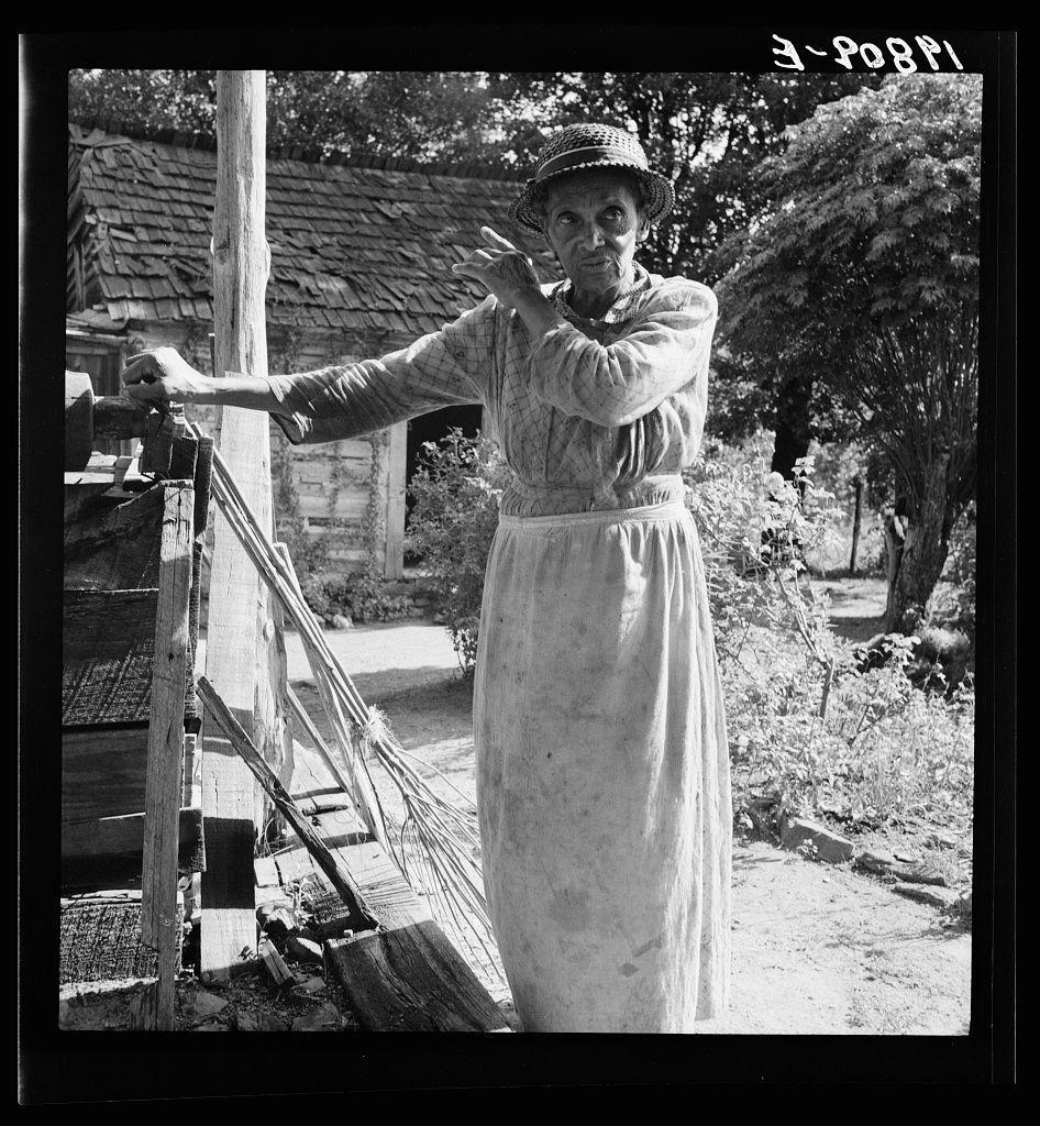 The image is a black and white photograph of an elderly woman standing outdoors, performing what appears to be the motion of throwing something. She wears a light-colored dress with rolled-up sleeves, indicative of practical attire for domestic or agricultural work. A straw hat sits atop her head, providing shade from above. The backdrop reveals rural surroundings featuring rustic buildings, dense foliage, and possibly a garden setting, suggesting a farmstead environment.

The photograph is labeled "3-PO8PI" at the top right corner, likely an internal cataloging code used by the photographer or archive to identify this particular image within their collection. It's part of Dorothea Lange’s work during the time when she documented various aspects of American life and society through her lens.

The photo captures a moment in the daily life that may be indicative of Depression-era conditions, which is further supported by additional information found at https://images.loener.nl/DorotheaLange/full/6495/6495b7e4ba25398d90c4f734.jpg. This link suggests a historical context where Lange’s photographs were used to document the socio-economic conditions of rural America, particularly during and after the Great Depression.

The image is framed by its dark edges, drawing focus onto the central subject with no distractions from peripheral details. The composition's clarity combined wi [...]