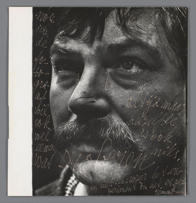 The image is a black and white portrait of an individual with dark, wavy hair. The person has prominent eyebrows, thick lashes on their eyelids, and visible fine lines around the eyes suggesting maturity or frequent expression. There are writings in cursive across various parts of the photograph; however, they appear to be non-English letters which could indicate a foreign language or artistic style rather than coherent text.

The background is plain with no distinguishable features aside from what appears as small droplets near the individual's nose and lips—these might represent tears or perhaps an artistic detail. The overall tone of the photo gives it a dramatic, possibly intense feel due to its monochrome palette and expressive subjects. There are some visible specks on the surface that resemble dust particles in the air around the subject.

The image seems like a piece from an artist's series given its unique style and presentation; however, without additional context or knowledge of the specific work this photograph is associated with, it remains a singular representation rather than part of a larger collection.