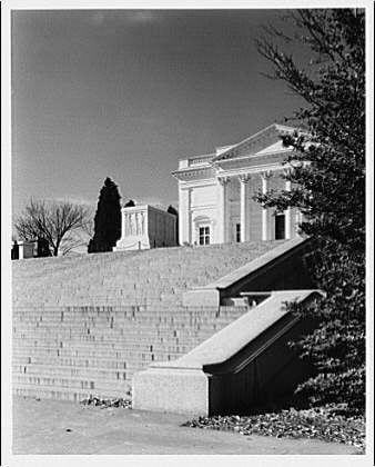 The image is a black and white photograph depicting an architectural structure, which appears to be the Tomb of the Unknown Soldier at Arlington National Cemetery. The building has classical design elements such as columns and pediments, suggesting its importance or commemorative purpose.

A stone staircase leads up towards this structure on one side, while another pathway runs alongside it. This part is partially obscured by a tree with visible foliage in the foreground. Another set of stairs can be seen to the right leading further away from the tomb-like building into an open area beyond.

The sky above appears clear and blue, indicating fair weather conditions at the time when this photograph was taken or represents what might typically occur there during that period (ca. 1920-ca. 1950).

Additional information on Arlington National Cemetery can be found through various online sources including historical records of American cemeteries maintained by organizations like The CWGC, which may contain further details about this specific site and its significance within the context of U.S. history.

The photographer who captured this image is identified as Horydczak, with an estimated lifespan between approximately 1890-1971 (Horydczak was a Polish-born American photography technician active from around World War I until well into the Cold War era). His work included documen [...]