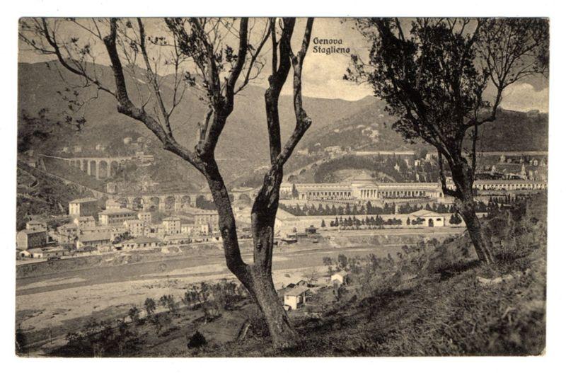 The image depicts a black and white vintage photograph showing the panoramic view of Genoa's Staglieno. In this historical photo, two prominent trees are situated in the foreground on an elevated terrain with sparse vegetation. The background reveals a sprawling townscape including what appears to be residential buildings clustered along terrains with varying elevations. Dominating the middle ground is a large structure resembling classical architecture with columns and symmetrical design elements extending across several levels.

Further back, atop undulating hills or mountainous regions, additional structures can be observed that seem less densely populated than the town below. The overall landscape suggests an early to mid-20th-century setting due to architectural styles and black-and-white photographic quality.

The upper part of the photo contains text in Italian: "Genova Staglieno," which identifies the location as Genoa's famous cemetery, known for its unique art nouveau architecture and notable burials. The image captures a serene yet historically significant view that may serve both as an artistic piece from this era or a historical document reflecting urban development during the time it was taken.

The photo bears signs of aging; minor tears are visible on its edges, suggesting it has been well-handled over decades. This gives the photograph character and evoke [...]