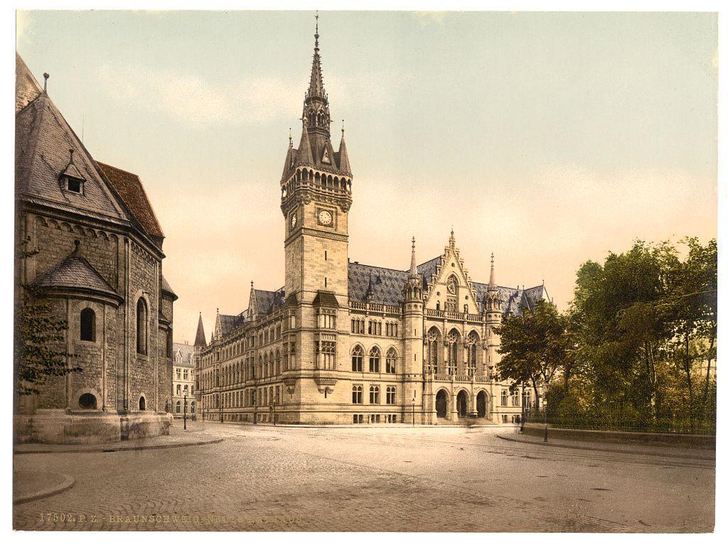 The image depicts a historic European town square with Gothic and Renaissance architectural elements, including steeply pitched roofs, ornate gables, and spires. The central structure is the New Town Hall in Braunschweig (Brunswick), Germany, as indicated by its distinctive clock tower topped with weather vanes and decorative stonework. This photograph captures a moment of quietude on an open square before modernity took hold; there are no visible people or moving vehicles, giving it a timeless quality. The image's sepia-toned coloration suggests age, likely dating from the late 19th to early 20th century when such prints were popular. The overall composition and historical context of this print offer insight into European urban life during that era.