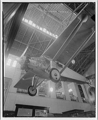 The image shows an old airplane suspended from the ceiling of a large indoor space, possibly a museum or exhibition hall. The photograph is in black and white, suggesting it could be several decades old. The plane appears to have been used for early aviation purposes, with its wings spanning across the width of the room above visitors below. There are visible structural elements such as beams supporting the ceiling structure from which the airplane hangs.

In addition to this visual description, there is contextual information provided that indicates a connection between the image and historical artifacts in Smithsonian Institution interiors. Specifically, it mentions "Spirit of St. Louis" and references Horydczak, Theodor (approximately 1890-1971) as someone associated with the photograph or its contents.

The dimensions given suggest that the negative was approximately eight inches by ten inches when developed, which is a significant size for photographic negatives during certain periods in history. This information helps to further date and contextualize the image within a specific historical timeframe related to early aviation and museum exhibitions of notable aircrafts like the Spirit of St. Louis.