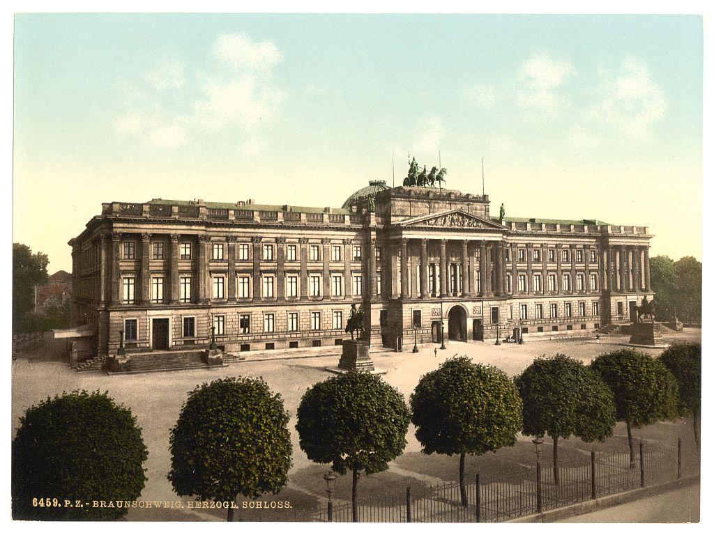 The image displays a historical building with classical architectural elements, featuring symmetrical facades and columns. It appears to be an important structure due to its grandeur and the presence of sculptures atop what seems like a pediment at one end. The surrounding grounds are neatly maintained, with trimmed bushes or topiaries in front of the building's facade on both sides, which suggests that this could be a significant public institution such as a palace or government building.

A small text is visible beneath the image and it reads "6459.P.Z.-BRAUNSCHWIEG-HERZOGL.SCHLOSS." This appears to indicate some form of cataloging system for historical photographs, possibly related to Brunswick (Germany) during Herzog Friedrich's reign. The overall quality and coloration suggest that this image is quite old, likely from the late 19th or early 20th century.