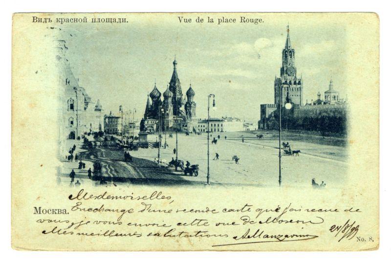 The image is a sepia-toned photograph, likely from the late 19th or early 20th century, depicting a bustling street scene in Moscow. The prominent feature of this urban landscape is St. Basil's Cathedral, with its distinct onion domes and baroque architecture standing out against a lighter sky background. Surrounding buildings exhibit classical European architectural elements such as towers and spires.

The photograph bears handwritten French text at the top that reads "Vue de la place Rouge," translating to "View of Red Square." Below this inscription is additional handwriting in cursive, which appears to be personal commentary or annotations from a collector's collection. The bottom left corner has printed Cyrillic script indicating it was part of a larger set with the number 8.

The overall condition of the image suggests age and wear, with creases and stains indicative of handling over time. This photograph captures a historical snapshot of Moscow during its period as the capital city of Russia.