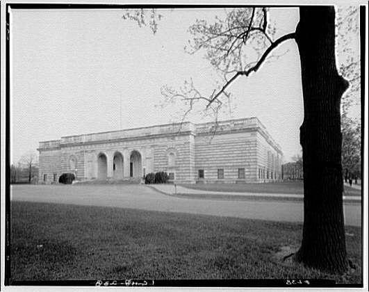 The image is a black and white photograph depicting the exterior of a stately, classical-style building. This structure has several notable architectural features such as columns supporting an entablature above its main entrance, which consists of three arches flanked by symmetrical rows of windows on either side. The façade displays horizontal lines dividing it into sections that emphasize its grandeur and formality.

A large tree stands prominently in the foreground to the right-hand side, providing a sense of scale against the building's backdrop. The lawn appears well-maintained with no visible objects or people, suggesting an atmosphere of quiet dignity and perhaps exclusivity for visitors.

The photograph is labeled "Freer Gallery" at the bottom left corner along with what seems like a date stamp from around 1920-50, indicating that this image could be part of historical documentation. The photo has visible signs of aging such as slight discoloration or wear on its edges, which are consistent with an old photograph.

In summary, the black and white image captures a moment in time outside what appears to be the Freer Gallery at around mid-20th century, showcasing classical architecture within a serene setting.