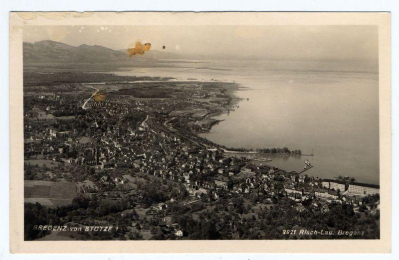 The image is a vintage black and white aerial photograph depicting the town of Bregenz, Austria. The landscape shows densely packed residential areas with roads intertwining through them, leading to what appears to be an industrial or commercial area along the waterfront where large buildings are visible near the shoreline.

In the foreground, there's prominent text "BREGENTZ von STOTZE" indicating that this image might have been created by a photographer named Stotze. A handwritten number "12970" is also present in the lower right corner which could refer to an album or collection within which it resides.

In the background, beyond Bregenz and its immediate surroundings, there's a large body of water extending toward distant hills or mountains. There are several small boats visible on this expanse, suggesting that despite being part of Austria, proximity to what appears like Lake Constance is evident from this vantage point.

The overall scene captures the serene yet bustling atmosphere typical of many European towns near significant bodies of water in earlier times.