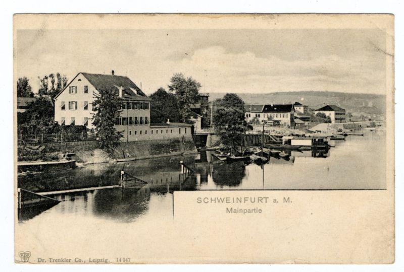 The image is a black and white vintage postcard depicting an early 20th-century scene of Schweinfurt, Germany. The main subject shows a river with boats docked along the right bank, leading to several buildings on both sides of the waterway. On the left side stands a prominent two-story building with large windows and a symmetrical facade typical of German architecture from that era. Further downriver, more structures are visible, including what appears to be industrial or commercial buildings adjacent to the riverfront.

The scene is set under an overcast sky, which contributes to the sepia-toned ambiance of the photograph. A prominent text overlay at the bottom reads "SCHWEINFURT a.M. Mainpartie," indicating that this part of Schweinfurt is referred to as its main district or central area. The postcard bears the mark "Dr. Trenkler Co., Leipzig, 14047" in the lower-left corner, suggesting it was printed by Dr. E. Trecker's Company based in Leipzig.

The condition and wear on the card indicate age, with visible creases and a slightly worn border typical of postcards that have been handled over time or stored without care. The image captures historical architecture alongside water transportation infrastructure, which could be indicative of Schweinfurt’s role as an industrial town during its active period in German history.

Additional information about this type of photogr [...]