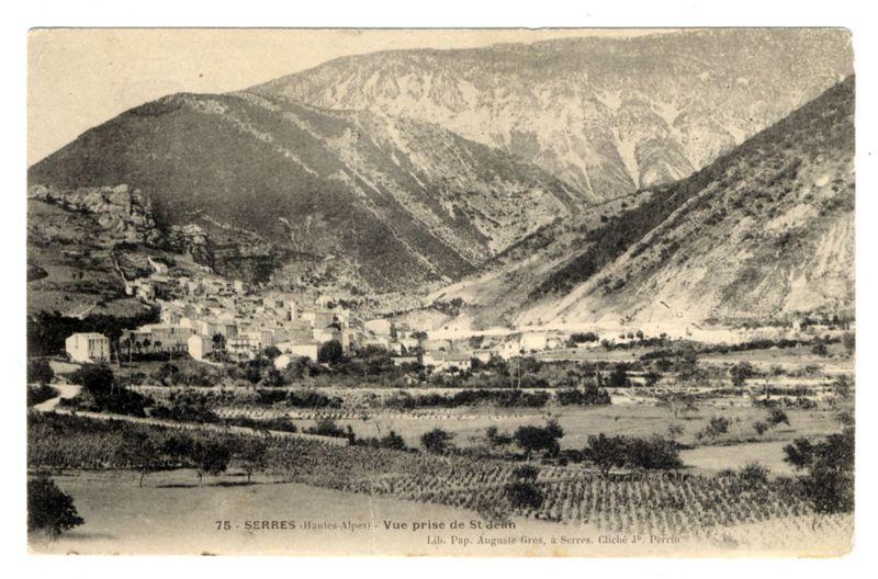 The image depicts a historical black and white photograph of the village Serres in Hautes-Alpes, with vineyards sprawling across terraced hillsides. Majestic mountains rise majestically behind the settlement. The photo bears text indicating its origin as "Vue prise de St-Jean," or "View from Sainte-Jean." It credits Father Auguste Gros and includes a reference to Llibre Páp., referring to what appears to be papal literature, hinting at religious significance in this depiction of the region. The terrain is rugged yet fertile for agriculture, suggesting a deep historical connection with viticulture or wine production.