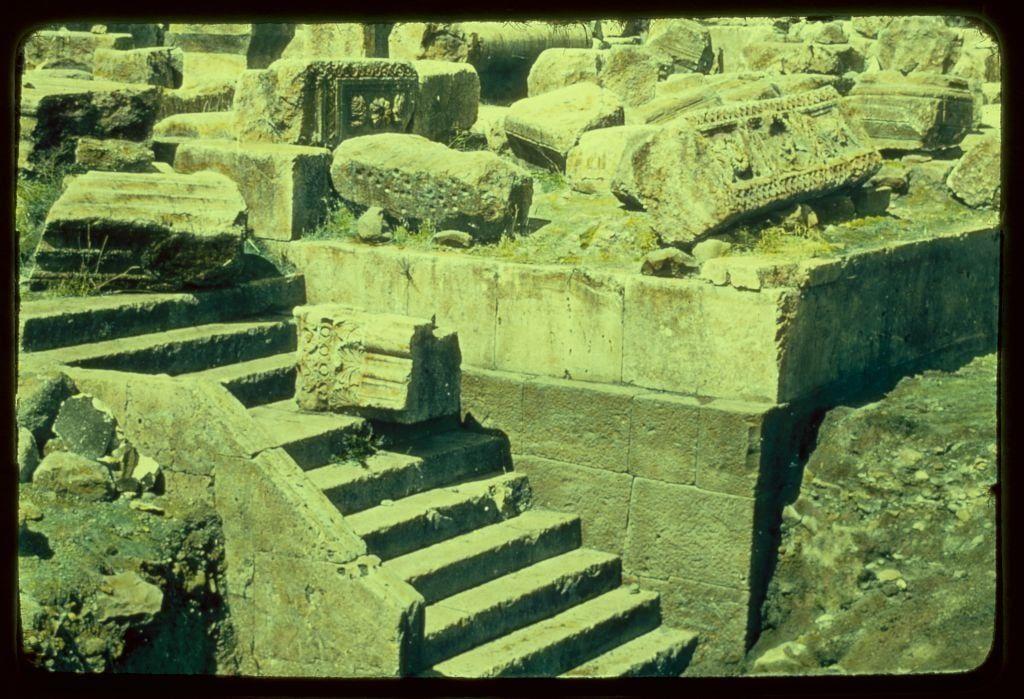 The image depicts a scene of ancient ruins, featuring weathered stone structures and scattered large blocks that appear to have once been part of larger edifices. Among these remnants are stairs leading upwards from the bottom left corner into what could be an archaeological site or historical excavation area.
Additional information about this image can be found in "Around the Sea of Galilee: Capernaum, ruins, eastern stairway between 1950 and 1977," suggesting that it was taken during a period when such sites were being explored. The Matson Photo Service is credited with capturing the photograph on film measuring two inches by two inches in size.
https://images.loener.nl/g-eric-and-edith-matson-photographs/full/691e/691ea072450e57a2674b96cb.jpg