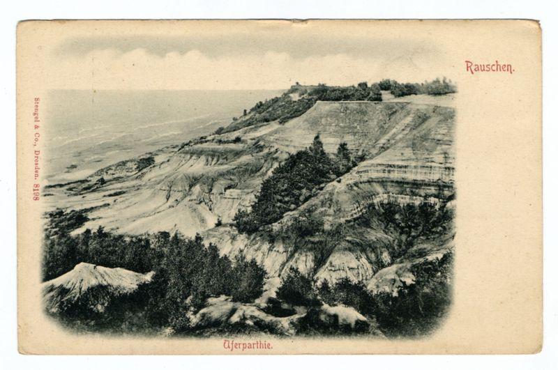 The image is a black and white photograph of an expansive landscape, possibly from the early to mid-20th century judging by its style. It features rolling hills or terrains with various elevations showcasing exposed earth layers that hint at geological activity such as erosion or tectonic shifts. The terrain appears barren in places but has clusters of trees indicating pockets where vegetation is more abundant.

There are no visible signs of modern infrastructure, suggesting a rural or natural setting rather than an urban landscape. Notable features include the stratification on the hills and what seems to be a forested area at the higher elevations.

The photograph includes text in German; "Rauschen" possibly indicating either a location name or perhaps the title of this particular view within the terrain shown, which translates as 'Rush' from English. The term could suggest rapid flow watercourses across such terrains if it was once part of an active riverbed. There's also another inscription "Überpartie," translated to mean 'over party,' possibly referring to a side or portion viewed above.

The photograph seems like a postcard, with the company name at the bottom left corner: Stiegel & Co., Dresden, and on top right "Rauschen." These markings suggest it was produced by a German photography studio. The image has some signs of aging such as creases and slight discolorat [...]