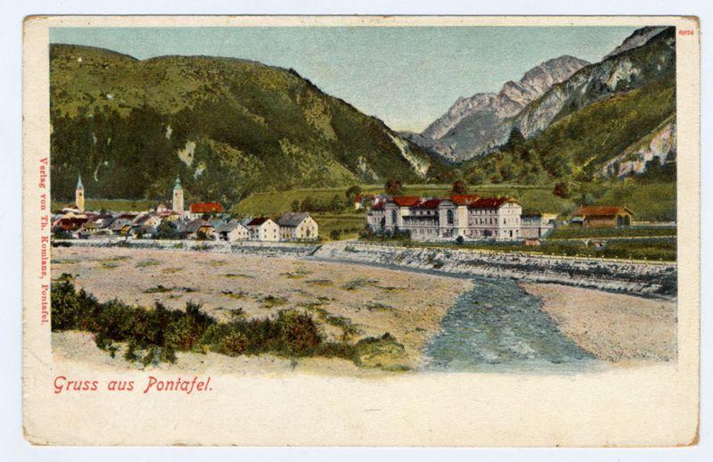 The image depicts a picturesque landscape featuring rolling hills and mountains in the background, with lush greenery adorning their slopes. In the foreground is a tranquil river meandering through what appears to be a rural or semi-rural setting. Alongside the riverbanks are several buildings including houses with red roofs, some of which have prominent chimneys, suggesting residential areas. There's also an imposing building that stands out due to its larger size and architectural style, possibly indicating it serves as a community center or town hall.

In the midst of these structures is what appears to be a church spire reaching towards the sky on one side, adding a touch of historical charm to the scene. The foreground features more barren land with sparse vegetation, which could indicate agricultural activity in some areas. Overall, this postcard captures an idyllic and serene rural environment, possibly from Europe based on architectural styles.

The image is labeled "Gruss aus Pontafel" at the bottom left corner, translating to "Greetings from Pontaful," hinting that it represents a town or village by that name. The overall impression of this postcard exudes tranquility and natural beauty, typical of a European countryside scene during an earlier period when such postcards were popular for communication purposes.