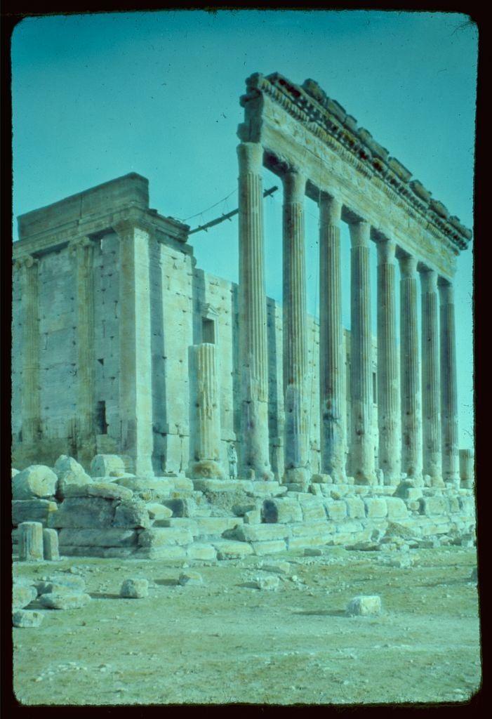 The image depicts the ruins of a classical Greek temple, showcasing its well-preserved columns and architectural elements. The structure appears to be an ancient edifice with remnants such as broken blocks scattered around the site. It stands amidst what seems like arid landscape, indicative of desert-like surroundings or historical sites in dry regions.

This photograph is part of the Eric and Edith Matson photographs collection at Loe-Ner. There are additional details about this image can be found from Damascus to Palmyra, highlighting its origin within a series that captures various archaeological locations across these areas during specific years ranging between 1950-77.

The photo is attributed to the "Matson Photo Service," indicating it may have been taken by or for their photographic organization.