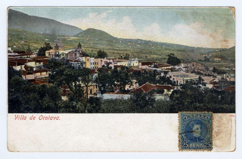 The image is a vintage postcard depicting the town of Villa de Orotava. In the foreground, red text reads "Villa de Orotava," indicating the location featured on the card. The upper right corner displays a blue postage stamp with an illustration of a person's face and the inscription "Espana" along with denomination details "25 CENT 25". The scene is set against a backdrop showing buildings, likely residential houses in shades of white, pink, yellow, and red hues, interspersed among greenery. A church or other significant structure stands out due to its height and distinct architecture. In the distance, rolling hills with patches of crops are visible under an overcast sky. The overall tone suggests historical significance, as evidenced by the age of the postcard and the stamp's design indicative of a past era.