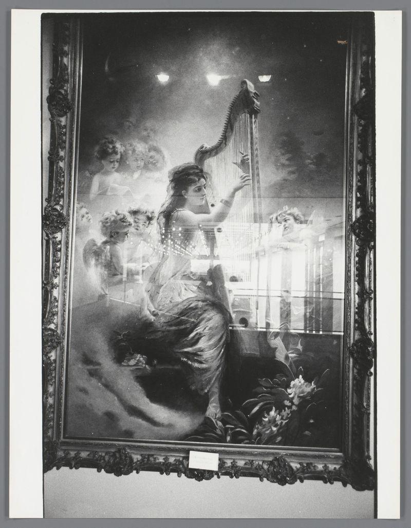 The image is a black and white photograph depicting an ornate framed painting. The central figure in the artwork appears to be a woman dressed elegantly, seated while playing a harp with her right hand on the instrument's neck. Her left arm extends outward as she looks towards something beyond the canvas. She has long hair styled up from which curls cascade down. Surrounding the main subject are ghostly or ethereal figures that resemble cherubim, adding an otherworldly quality to the scene.

The background behind these figures is blurred with hints of light and darkness, creating a sense of depth and mystery. The painting's ornate frame has elaborate carvings typical of classic European art styles, suggesting it may be from a bygone era or styled as such for its aesthetic appeal.

In front of this painted scene, the actual photograph capturing the image is displayed on a white background with what appears to be a card placed at the bottom right corner. The card has some text but isn't legible in the provided resolution. Overall, the composition creates an intriguing blend between reality and artistic interpretation.