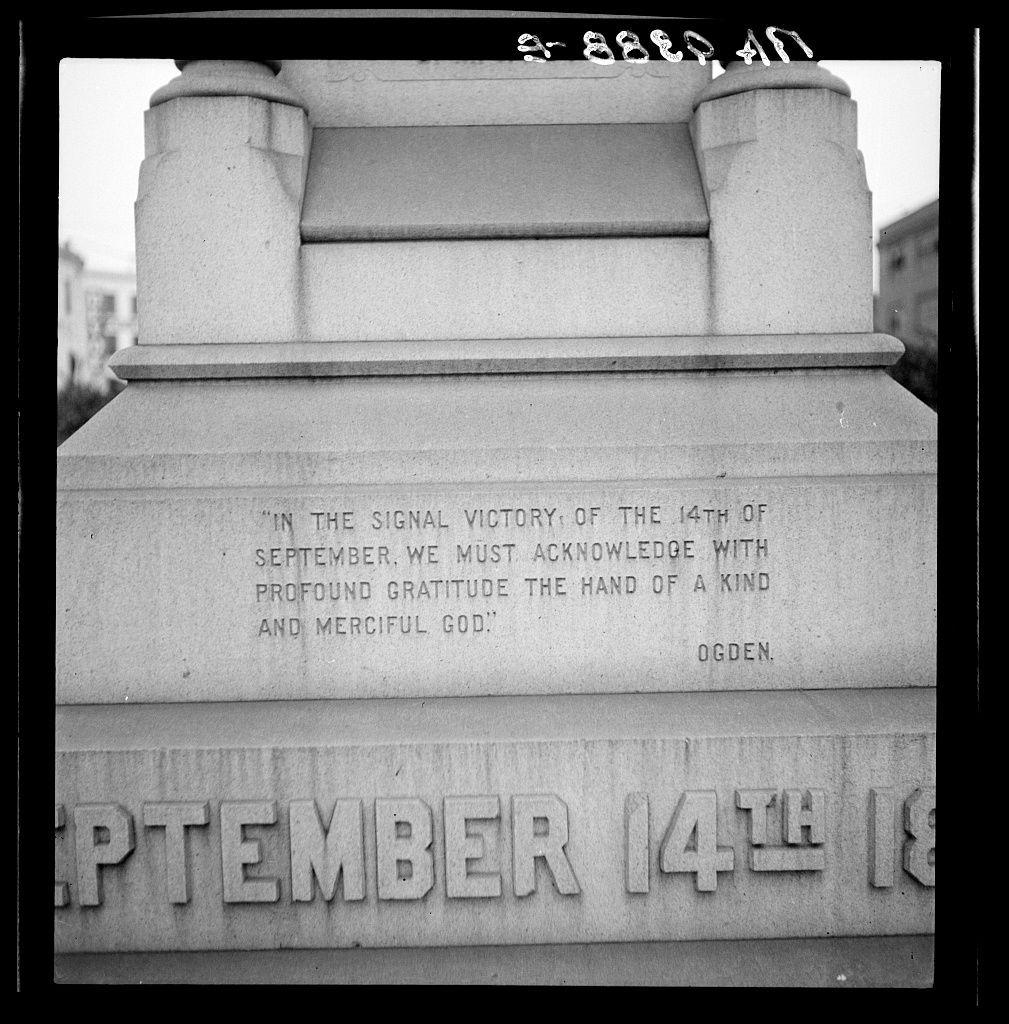 This black and white photograph depicts a portion of an inscription on the base of a monument. The text, set in uppercase letters, reads: "IN THE SIGNAL VICTORY OF THE 14TH OF SEPTEMBER, WE MUST ACKNOWLEDGE WITH PROFOUND GRATITUDE THE HAND OF A KIND AND MERCIFUL GOD." Below this message is another line that says "SEPTEMBER 14th" and the name "OGDEN," which seems to be part of a signature or dedication. The monument appears to have an architectural design, with blocks stacked atop one another, supporting a smaller block on top where the inscription is located.

The background shows parts of buildings, suggesting that this photograph was taken in an urban setting. There's also a watermark-like text "g-825041" at the top edge and bottom right corner, likely indicating either the photographer or image cataloging information. The overall impression is one of historical commemoration, possibly related to civil rights history given its reference to race prejudice mentioned in the linked source from New Orleans, Louisiana.
