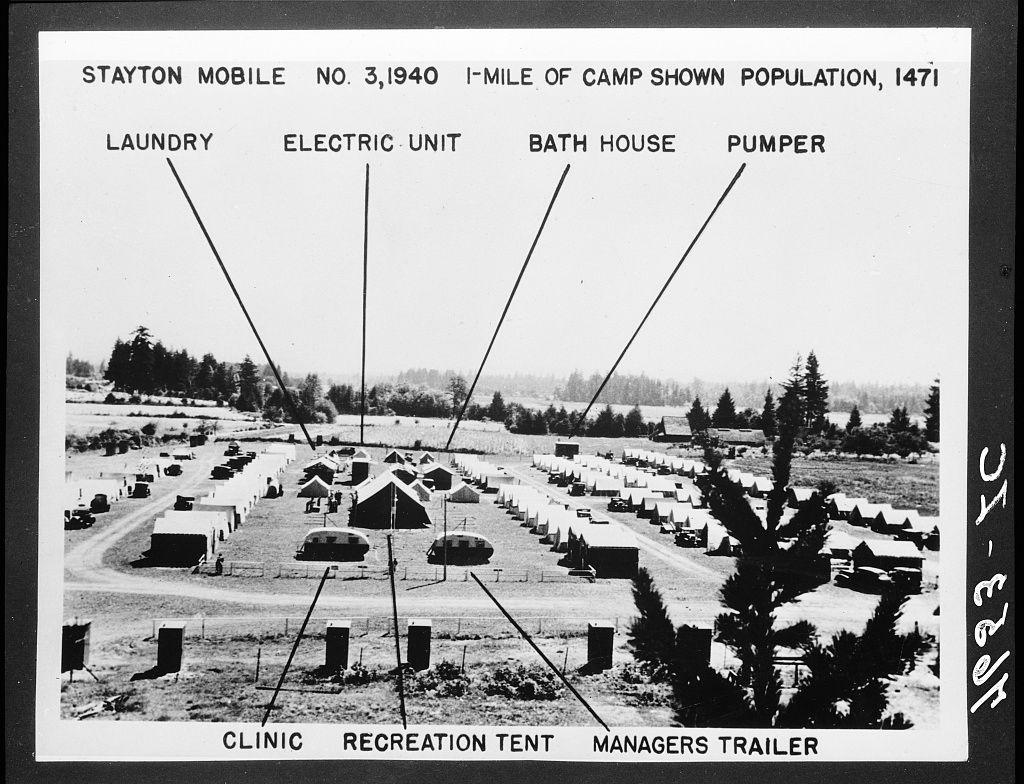 The image is a black and white photograph of an outdoor military camp setting, labeled "STAYTON MOBILE NO. 3,1940 I-MILE OF CAMP SHOWN POPULATION, 147I". The photo depicts various facilities associated with the mobile unit identified in its title.

There are several structures marked on the image: 
- A Laundry building
- An Electric Unit (presumably a power generator or electrical distribution hub)
- A Bath House for sanitation and hygiene purposes
- Pumpers, likely referring to water pumps used by camp personnel

Below these facilities is a row of mobile homes with roofs pitched towards the sky. These could be barracks where soldiers were stationed.

Surrounding this central area are numerous white tents labeled in relation to their purpose: 
- Clinic for medical services,
- Recreation Tent presumably housing recreational activities or social gatherings, and
- Managers Trailer which likely housed camp management personnel

Additionally, there is a line of vehicles marked "MANAGERS TRAILER," suggesting that the mobile units were meant for temporary occupancy.

The background shows an expansive field with sparse trees. The image captures a moment in time from World War II era military life, emphasizing organization and preparedness within this makeshift camp setting.