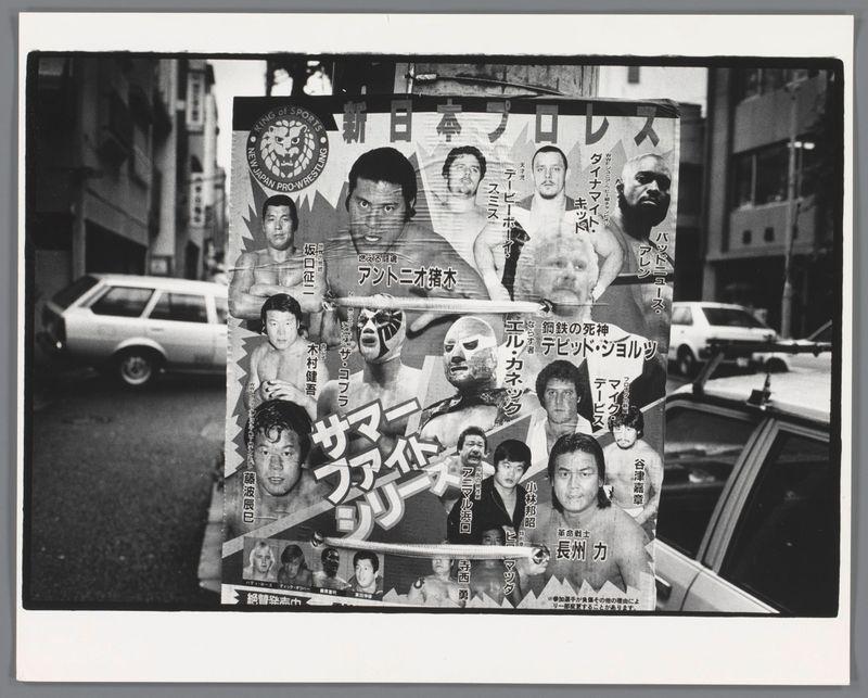 The image displays a collage of black and white photographs related to Japanese professional wrestling, with prominent text in both English and non-English languages. Central is the phrase "KING OF SPORTS," followed by a circular emblem reading "NEW JAPAN PRO-WRESTLING" around an illustration resembling a lion's head. Surrounding this central image are various photos of individuals, presumably wrestlers, each depicted against different backdrops such as urban streets and other promotional materials with Japanese text. The collage is framed on the left side where it appears to be taped or hung up in front of buildings, with parked cars visible through gaps between the hanging items. Notable features include a knife angled over one section at the top right corner, suggesting an element of danger or excitement often associated with wrestling events.