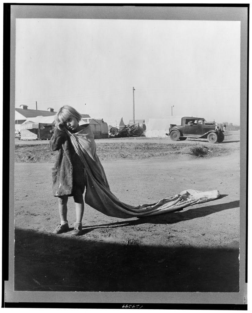 The photograph is a black and white historical image depicting an individual in what appears to be rural or semi-rural conditions, with structures that resemble farm buildings visible in the background. The person seems to be engaged in some activity involving textiles on the ground. In the foreground, there's another figure draped in fabric, possibly indicating labor-intensive work associated with textile production or agricultural tasks like cotton picking.

The setting appears rustic and somewhat desolate, suggesting a rural environment that could have been common during periods of hardship such as the Great Depression. The absence of modern infrastructure and vehicles hints at an era where transportation was more primitive and reliant on manual labor for daily activities.

Given the context provided by Young Cotton Picker Kern County Migrant Camp in California (https://images.loener.nl/DorotheaLange/full/6495/6495b8d4ba25398d90c5150c.jpg), it is reasonable to infer that this photograph may be related to the lives of migrant workers, specifically those involved in cotton picking during a time when such camps were prevalent. The attire and condition depicted suggest hardship or poverty.

The specific individual's identity remains undisclosed, focusing instead on their occupation as portrayed by Dorothea Lange, known for her work documenting the Great Depression and its  [...]