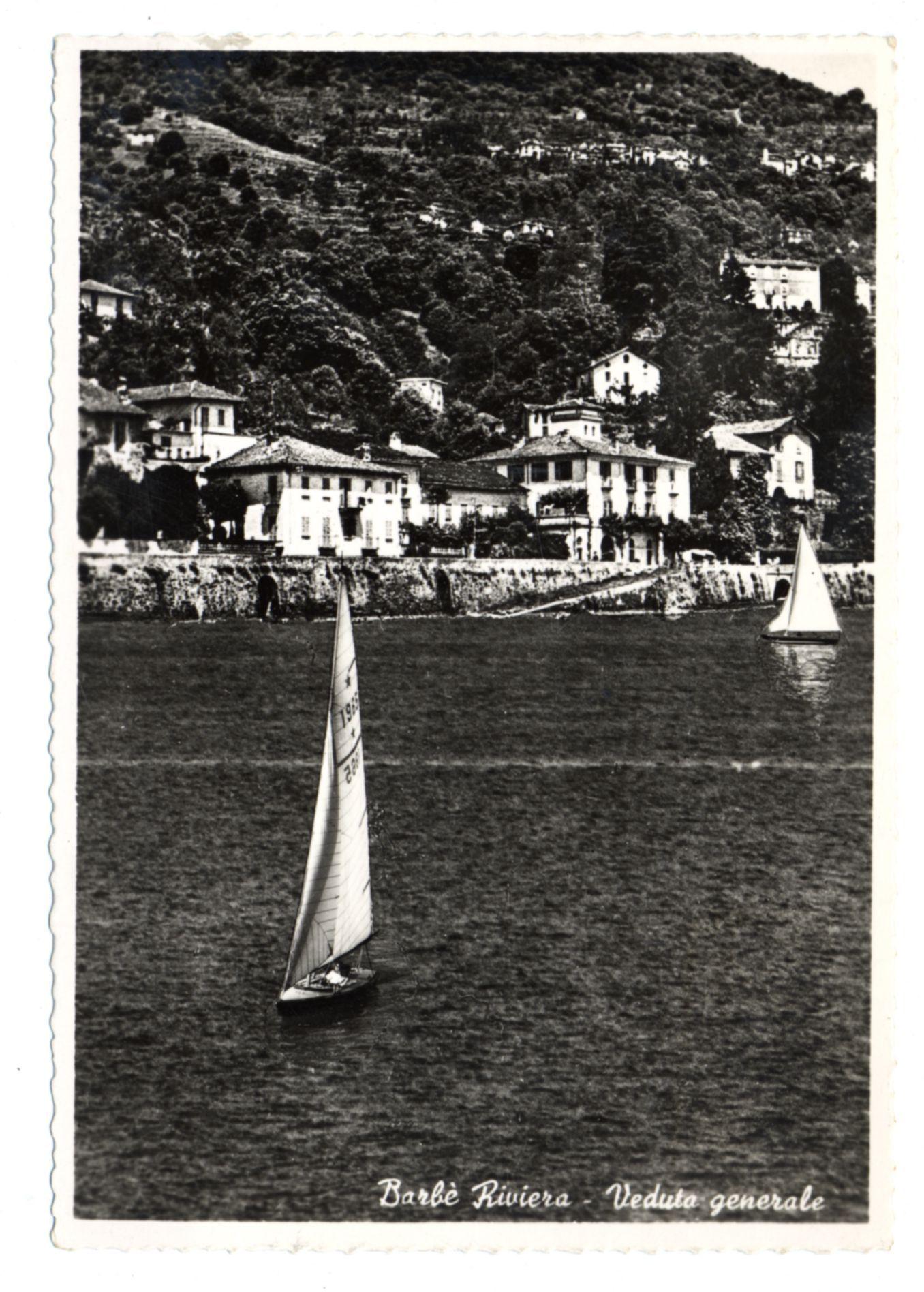 The image displays a vintage black and white photograph depicting a serene coastal scene. In the foreground, there is a body of water with two sailboats; one closer to the viewer has its sails fully unfurled while another in the background appears smaller due to distance. The middle ground features an array of traditional European-style houses perched on a gently sloping hillside. These buildings are characterized by their tiled roofs and white walls, suggesting a Mediterranean influence. Vegetation is scattered throughout the landscape, indicative of hilly terrain possibly typical for regions such as Barbe Riviera in Italy or similar coastal areas.

The image has an aged look with faded tones and graininess that suggests it could be several decades old. The text "Barbe Riviera - Veduta generale" indicates a general view from Barbe Riviera, hinting at the location being of historical interest possibly for tourism or cultural significance in its time. There's also mention of Ferro Candilera which may refer to another entity associated with this locale.

The watermark suggests that more detailed information about the image can be found online via provided links and references, adding context on where further exploration is possible.