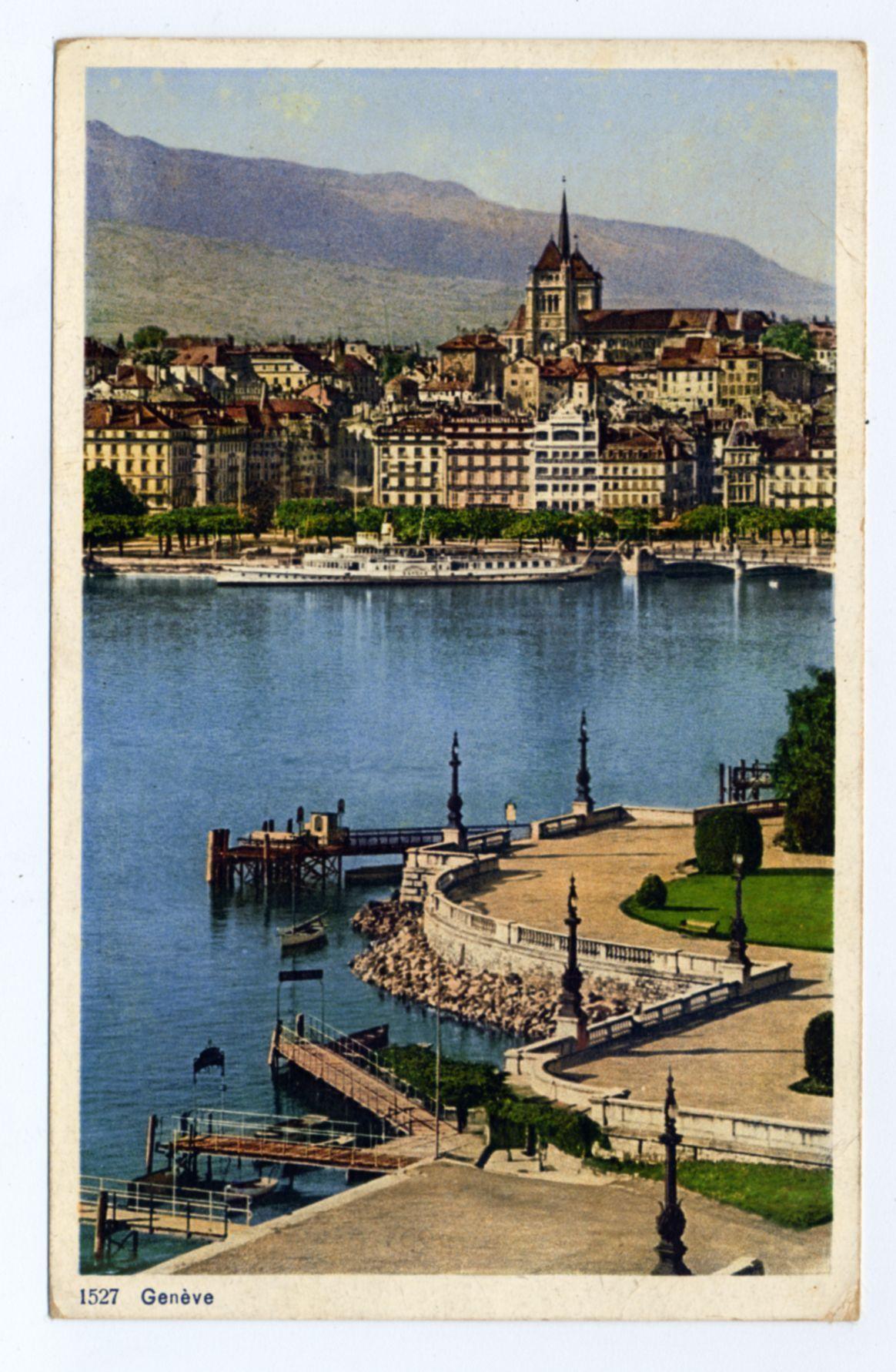 The image depicts a picturesque lakeside view of Geneve, Switzerland. The foreground shows a well-maintained promenade with lampposts and benches alongside the lake's edge where several boats are moored at wooden docks. A metal pier extends into the water, leading to what appears to be an industrial or maintenance structure towards its end.

The middle ground is dominated by clear blue waters of Lake Geneva, reflecting sunlight on their surface. On one side of this body of water sits a cluster of historic buildings with ornate architecture and red-tiled roofs; these structures likely have significance as cultural landmarks within the city.

Beyond the urban skyline stands an imposing church or cathedral with spires reaching towards the sky, suggesting its prominence in local religious practices and community life. The background is framed by rolling hills that give way to a mountainous landscape under a clear blue sky scattered with wispy clouds.

The overall atmosphere conveyed through this image suggests calmness and beauty typical of Geneve's lakeside environment while also highlighting architectural elegance reflective of Swiss culture.