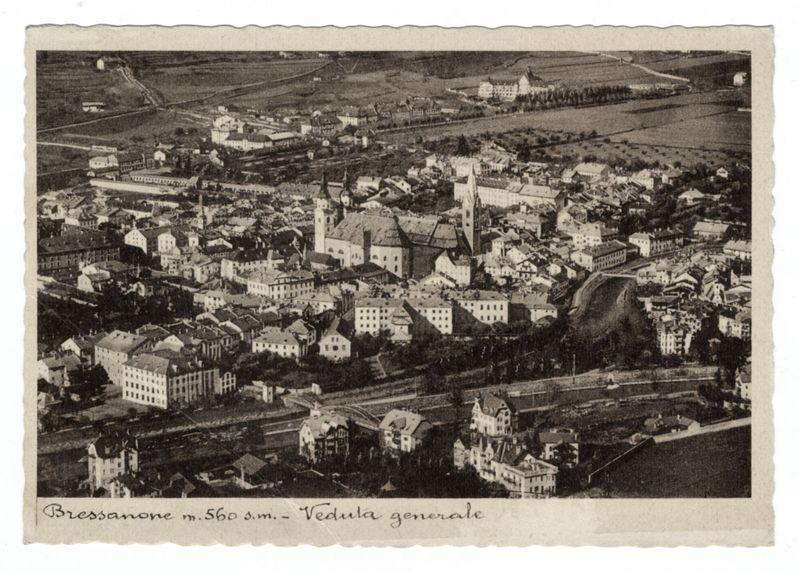 The image displays an aerial view of the historical town Bressanone, with a focus on its central area. Prominent in this scene is St. George's Cathedral (Cattedrale di San Giorgio), identifiable by its bell tower and large structure among other buildings. The photograph appears aged, suggesting it may be from the late 19th or early 20th century.

Below the aerial view of Bressanone stands a caption that reads "Bressanone m.560 s.m.- Veduta generale," indicating this is an overall overview of the town at approximately 560 meters above sea level. The image's monochromatic tone and texture suggest it might be from early photography or have been altered to resemble such a vintage aesthetic.

The surrounding landscape includes patches of greenery, possibly fields or parks, with more buildings dispersed across them. A river can also be seen flowing through the town, adding a natural element to this urban setting. The overall composition provides insight into Bressanone's historical architecture and its geographical layout within that time period.