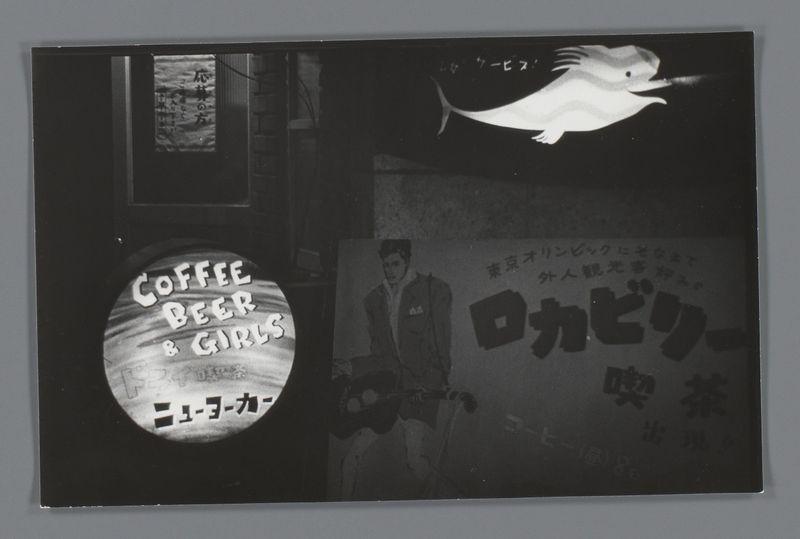 The image is a black and white photograph featuring two distinct signs. On the left side, there's an illuminated sign with Japanese characters that read "Coffee Beer & Girls" in English below it. The text is also accompanied by symbols such as beer bottles and coffee cups within circles. To the right of this sign is another one, larger and prominently displayed against a dark background, bearing similar Japanese lettering which translates to phrases like "coffee," "beer," "girls," among other words that are not fully legible in English.

In front of these signs stands a person wearing what appears to be military or uniform-style clothing. The individual is slightly turned away from the camera and looking toward something off-camera, with only their profile visible due to the angle at which they're photographed.

Above this scene floats an image of a stylized white fish in flight against the dark sky, adding a whimsical element to the composition. This could represent one of the services or themes advertised on the signs below it.

The photograph has been cropped into three separate panels with black borders framing each sign and figure individually. The overall impression is that this might be an image from a nightlife scene in Japan during the 1950s, as suggested by the accompanying text mentioning Uithangborden van nachtclubs (nightclub posters) in Japan, which correspo [...]
