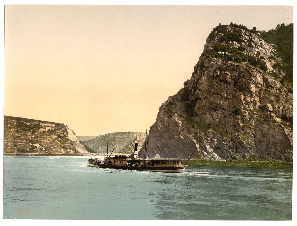 The image depicts a vintage scene featuring an old steamship traveling on calm waters, with the backdrop of rocky cliffs. The ship has multiple decks and appears to be transporting passengers or goods, as suggested by the presence of railings along its sides for passenger safety.

A notable feature in this landscape is a large cliff that rises dramatically from the river's edge, giving off an aura of grandeur and natural beauty. In the background, additional cliffs can be seen on both banks of the river, suggesting a picturesque yet rugged terrain typical of European rivers like the Rhine or Danube.

The water appears serene with gentle ripples indicating movement in calm conditions. The overall tone is warm, as indicated by the yellowish-brown hue that bathes the entire scene under what seems to be late afternoon sunlight.

At the bottom left corner, there's text inscribed which reads "THE LOE R I," a reference likely pertaining to the ship or location depicted within this histo