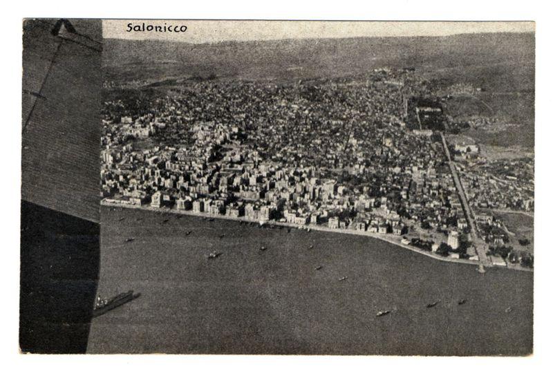 The image depicts an aerial view of a densely populated city, identified by the inscription "Salonicco" as Thessaloniki. The landscape is divided into various urban blocks with numerous buildings closely packed together, indicating a well-developed metropolitan area. There's a clear distinction between residential and possibly commercial areas based on building density and layout.

A wide body of water surrounds one side of the cityscape, hinting at its coastal location or proximity to an expansive harbor. Boats are visible in this expanse of water, suggesting maritime activity is part of the town’s character. The topography appears flat with no significant elevation changes within the urban space itself, which could be indicative of a planter development over time.

The black and white tone of the image suggests it's historical or at least an older photograph, capturing Thessaloniki before modern color photography became prevalent. This vintage quality adds to its historical value