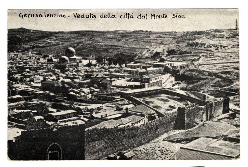 The image is a black and white historical photograph depicting an aerial view of Jerusalem. It showcases the ancient city walls enclosing various architectural structures, including what appears to be religious buildings with domes, indicative of significant cultural or sacred sites. The terrain surrounding the walled area shows undulating hills in the background. In bold cursive writing across the top left corner, it reads "Gerusalemme - Veduta della Città dal Monte Sion," which translates from Italian as "Jerusalem – View of the City from Mount Zion." This suggests that this image was taken during a time when the city's architecture and landscape had been largely preserved or untouched by modern development. The photo has an aged appearance, with visible creases and spots indicative of its age and handling over time.