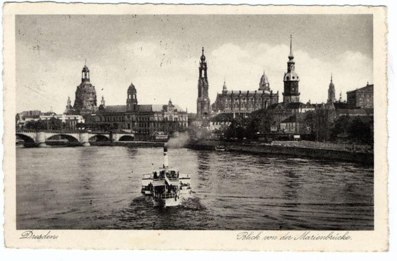 The image depicts a sepia-toned historical photograph of Dresden, Germany. It captures the majestic skyline of Dresden with several prominent church spires and buildings on the bank alongside a riverfront promenade. In the foreground is a steamboat navigating through calm waters, creating ripples as it moves forward. The boat appears to be carrying passengers or cargo and has multiple levels visible from this perspective. A bridge spans across the background over the waterway behind the church spires.

At the bottom left corner of the image, "Dresden" is inscribed in elegant script, indicating the city's name. Additionally, at the top right corner, another inscription reads "Blick von der MARIENBRUCHE," suggesting that this view was captured from a location known as Marienbrücke.

The overall appearance suggests an early to mid-20th-century photograph due to its black and white quality, texture, and style of writing. The image evokes the historical charm and architectural grandeur 