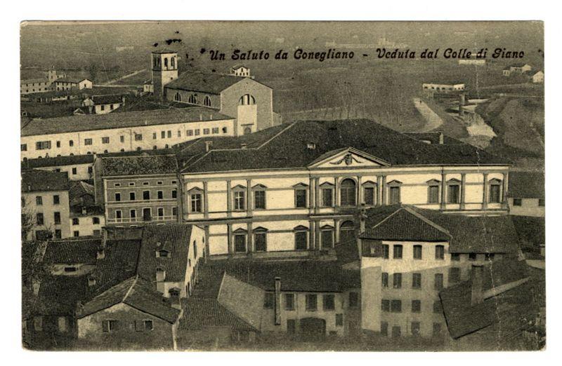 The image is a vintage black and white photograph depicting an aerial view of historical buildings. Prominent in the center are two notable structures with classical architectural elements such as arched windows, decorative friezes above these archways, and symmetrical facades. The larger structure on the right features a porticoed frontage with four columns supporting a triangular pediment.

Surrounding these central edifices are various other buildings exhibiting plain brick construction with simple rectangular windows. A river or stream meanders through the landscape in the background to the left, adding depth and context to the scene. The photograph is titled "Un Saluto da Conegliano - Veduta dal Colle di Gianc," suggesting it captures a view from a hill called Gianc towards an area of Conegliano.

The image appears aged with some faded areas and creases indicative of wear or physical handling over time, hinting at its historical significance. The overall composition provides i